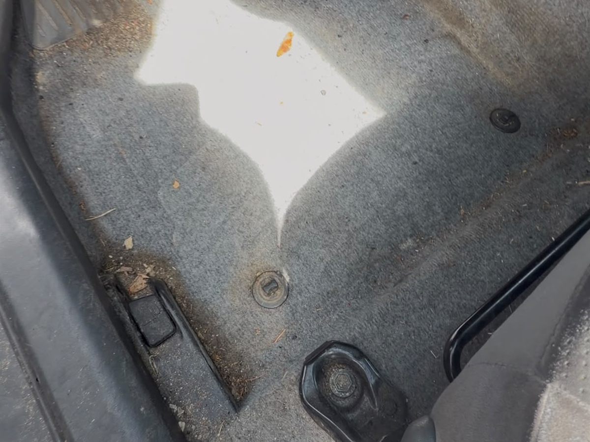 Car footwell before cleaning, with ground-in dirt and debris along the door sill
