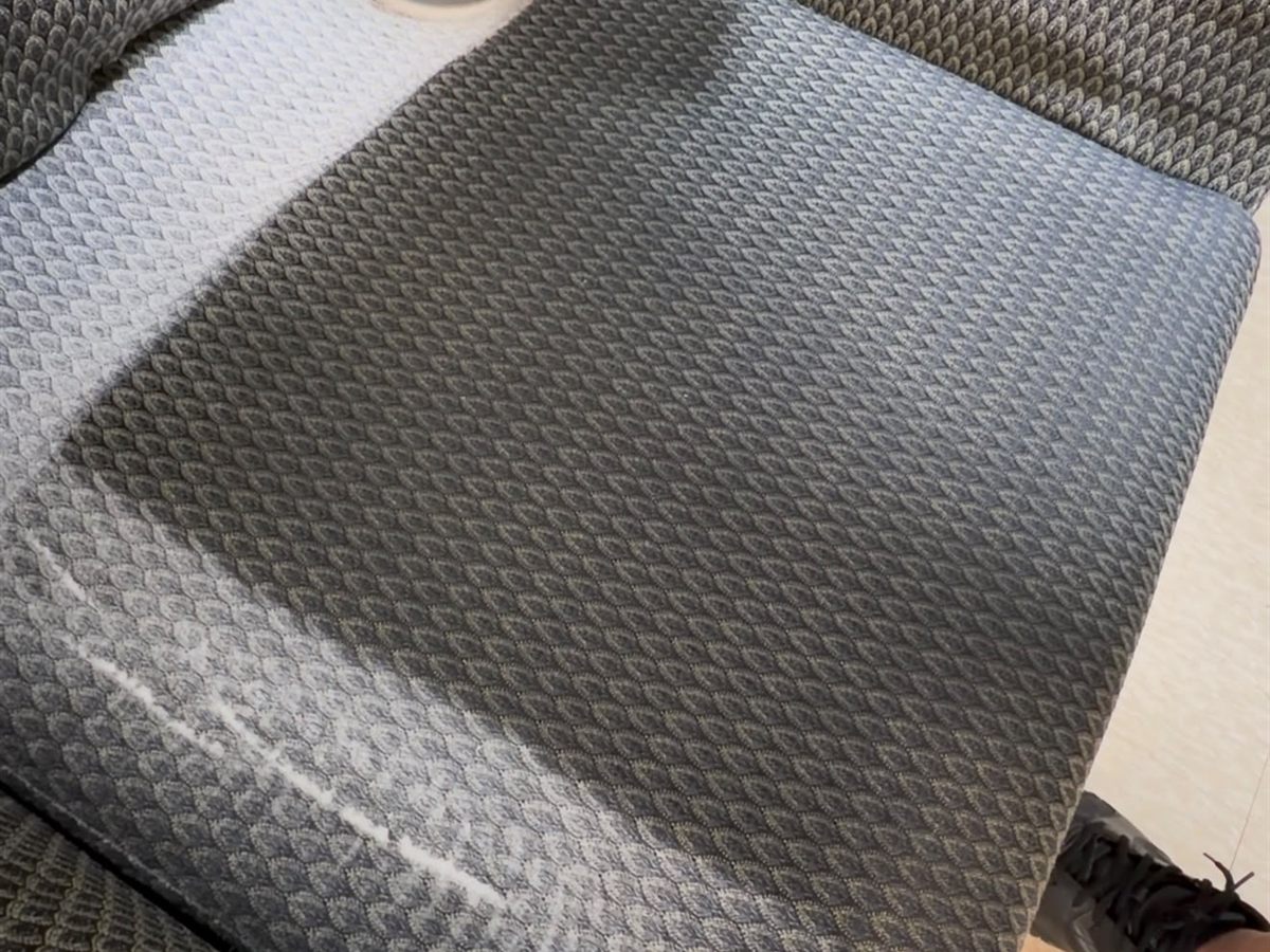 A grey upholstered seat halfway through cleaning: a light, clean band on the left against the darker soiled weave on the right